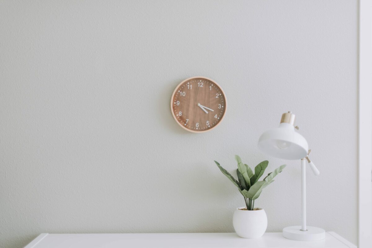 A photo of a white desk lamp, a plant, and an analog clock