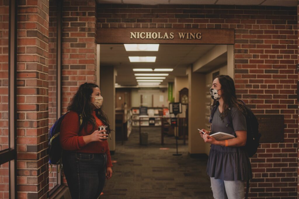 Two masked Wheaton students talking in Buswell Library