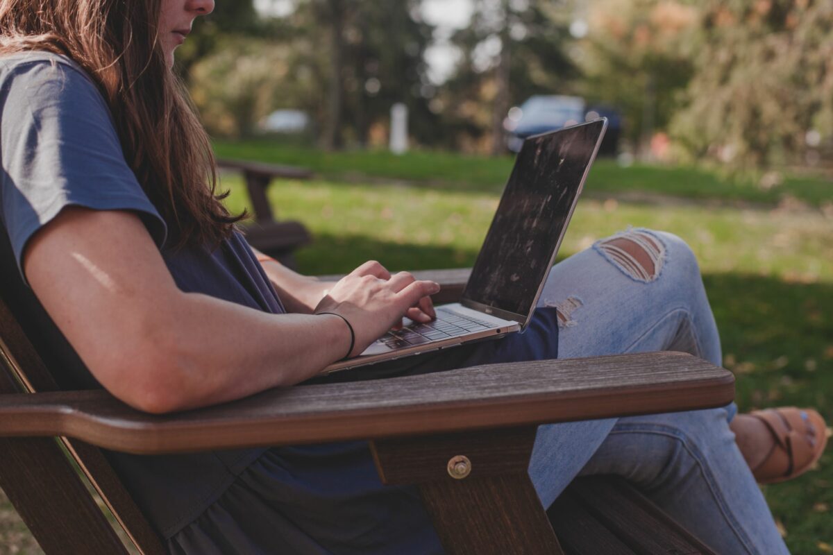 A photo of a college student typing on a laptop outdoors