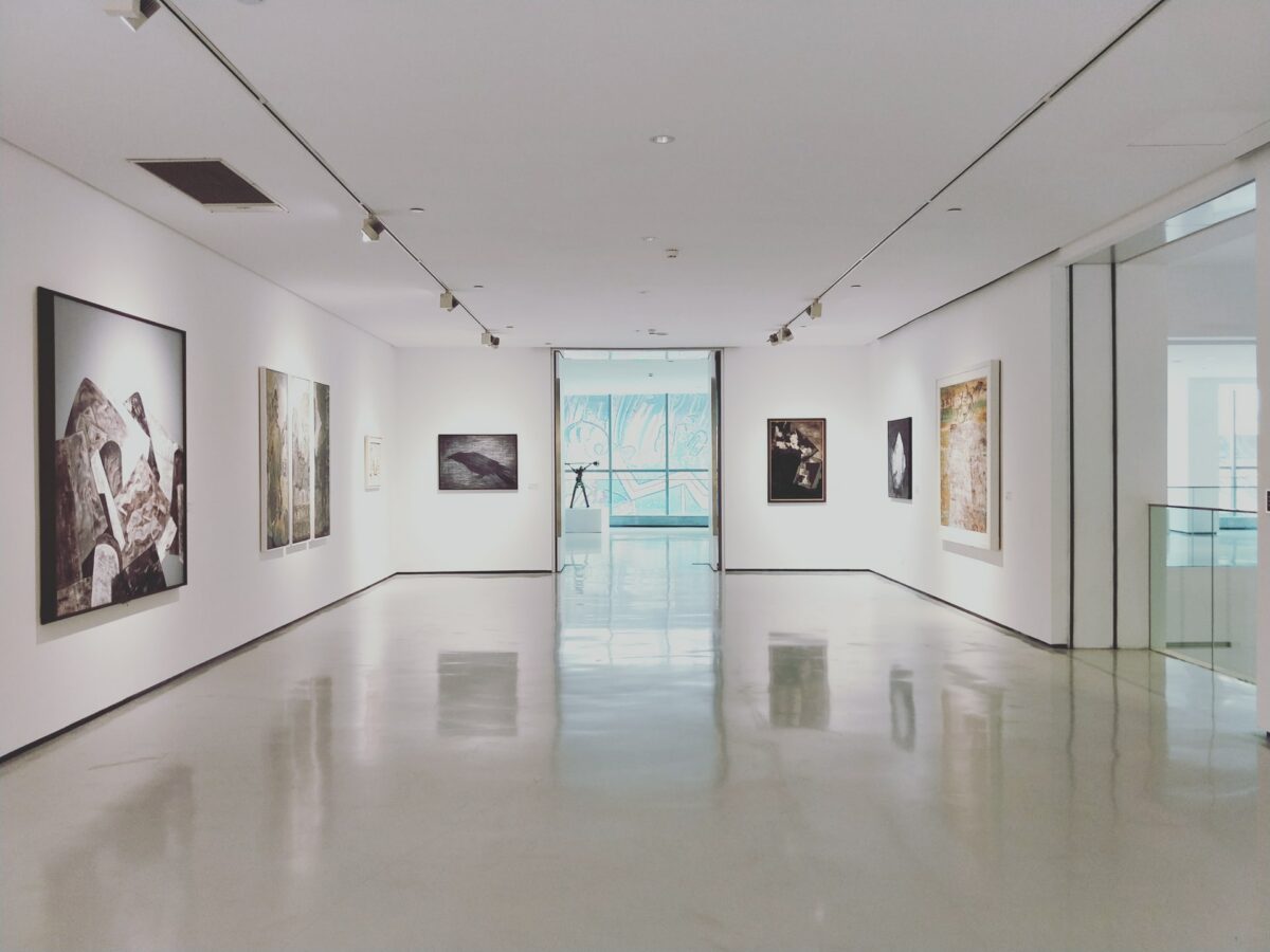 A photo of a minimalist white room of a museum with artwork on the walls