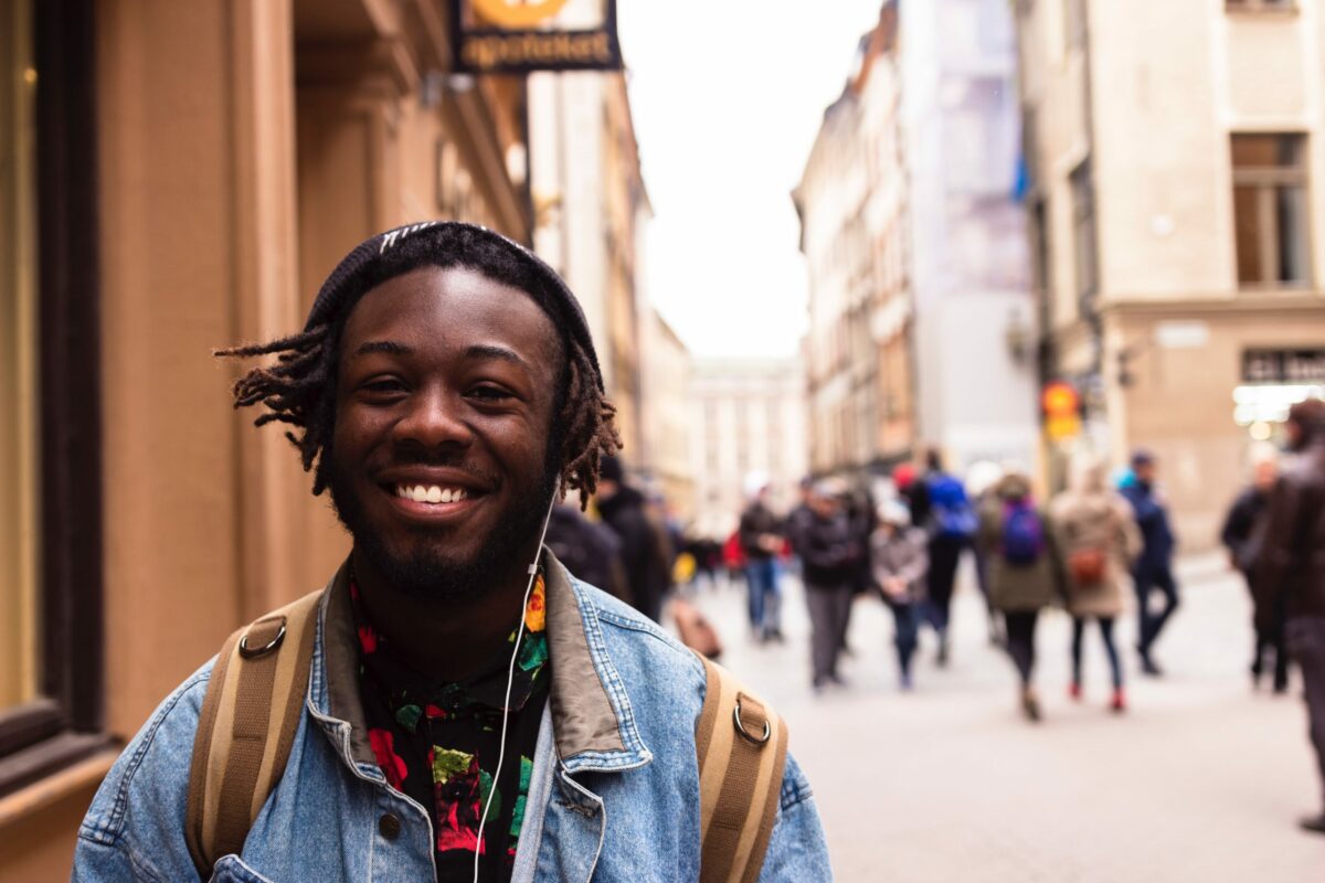 A photo of a young man on a city street wearing a backpack and smiling