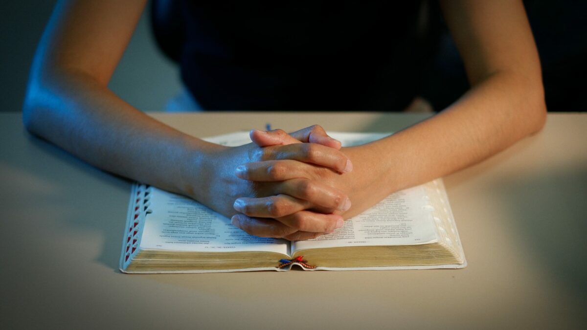 A photo of a young person's hands folded in prayer over an open Bible
