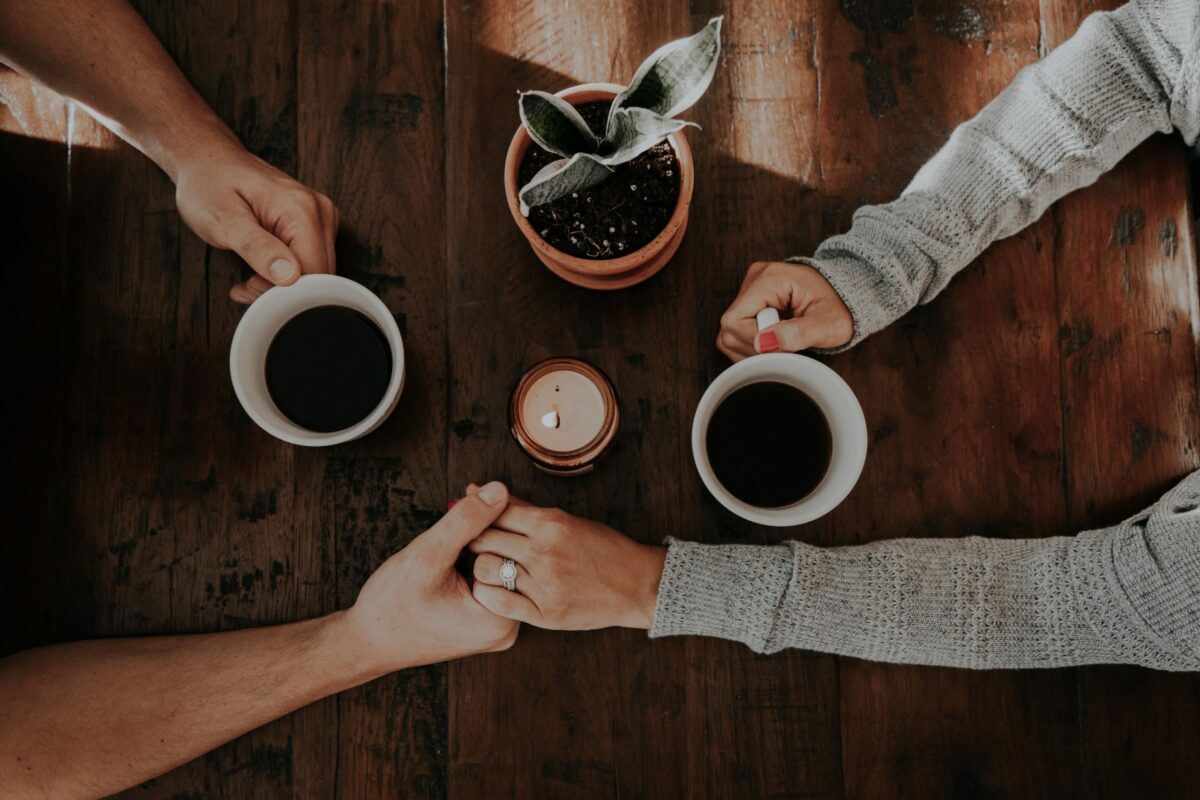 Two people hold hands around cups of coffee.